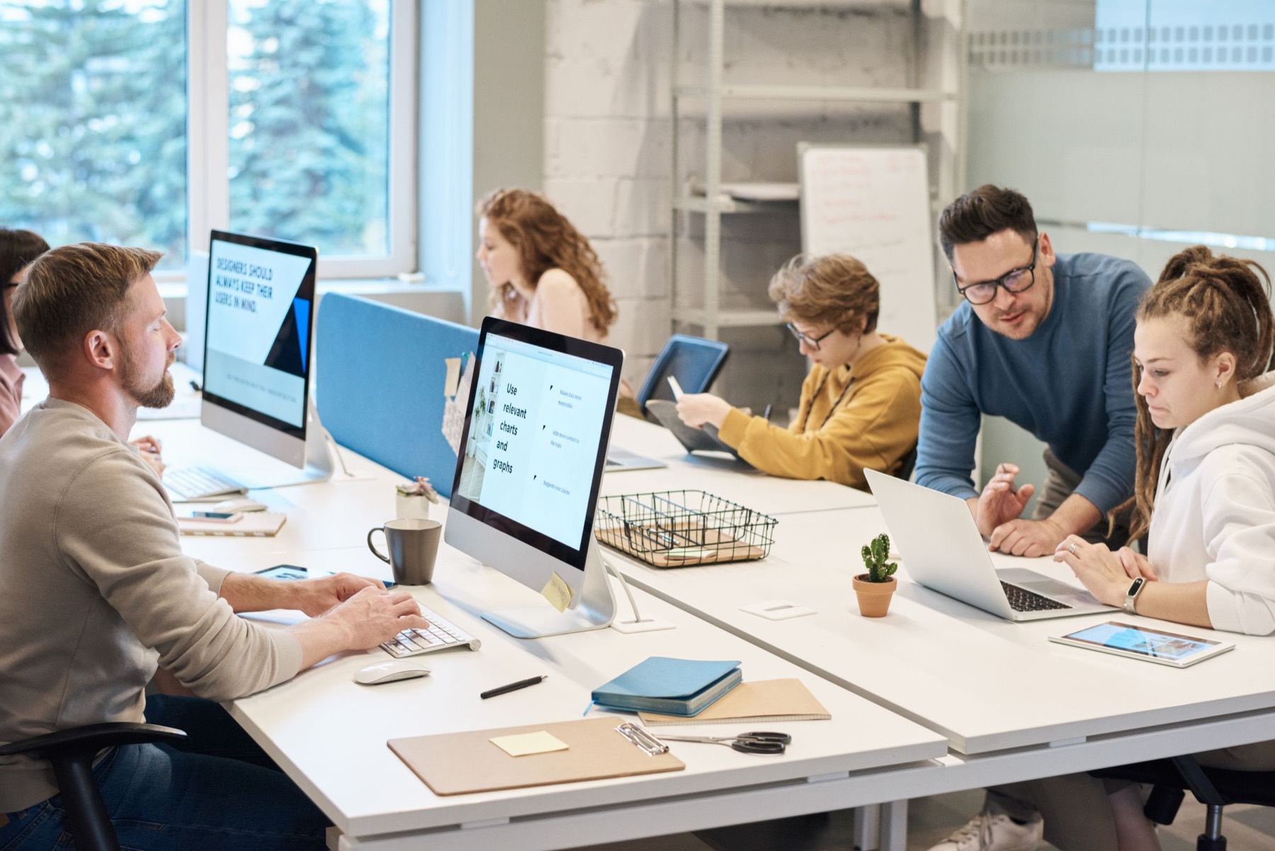 Colleagues working at desktop computers along a bright office desk row